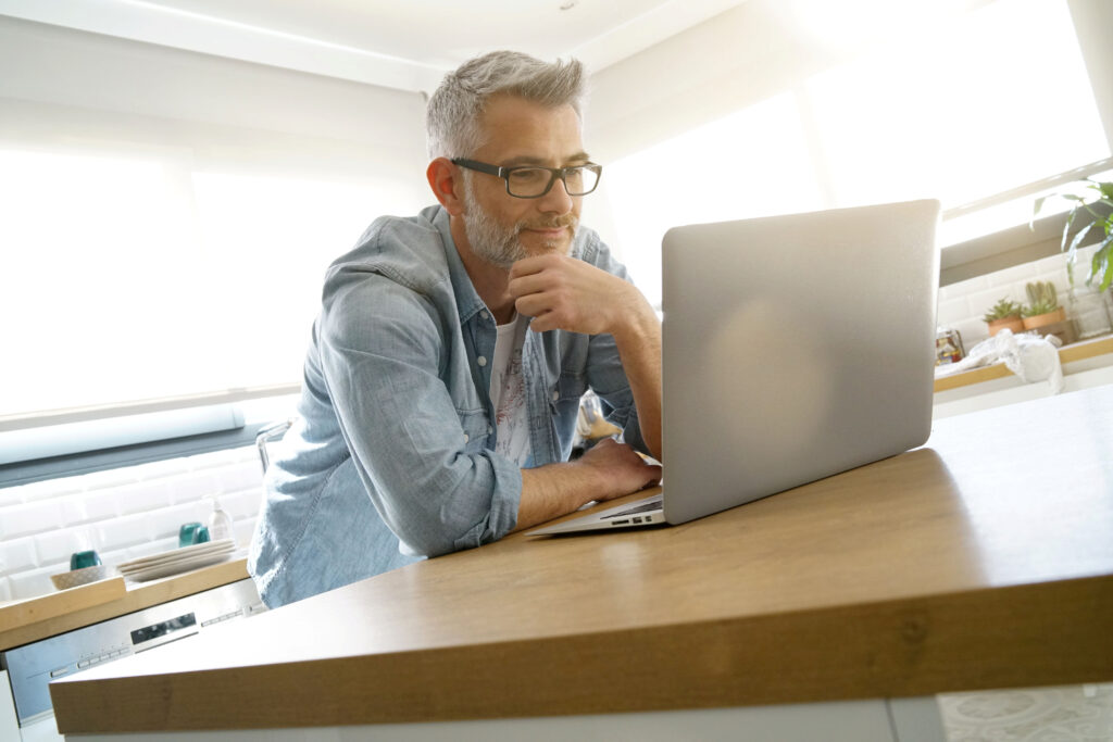 Mann steht in der Küche und arbeitet am Laptop