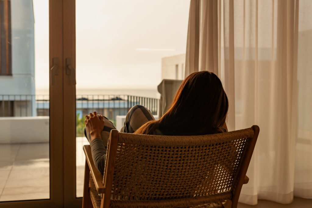 Frau sitzt vor Fenster und schaut sich den Sonnenuntergang an.
