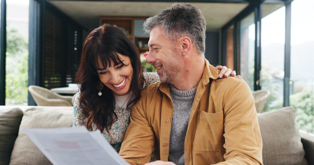 Ein Paar sitzt zusammen auf einem Sofa und schaut sich gemeinsam Förderungs-Unterlagen an.